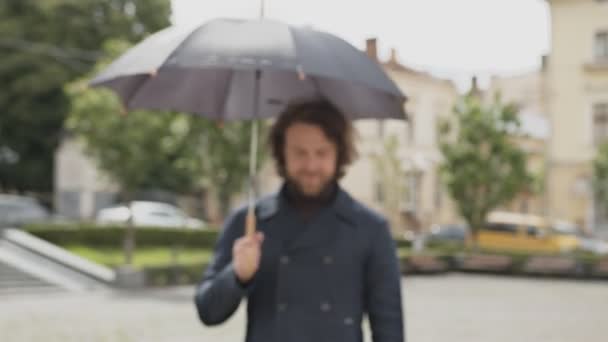 Focando a câmera em um jovem homem bonito com um belo sorriso e um guarda-chuva — Vídeo de Stock