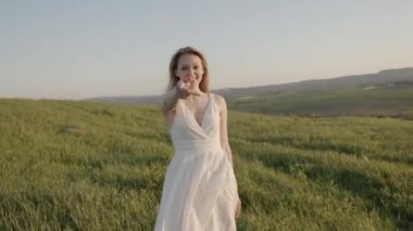Beyaz elbiseli mutlu kadın çayırda daireler çiziyor.