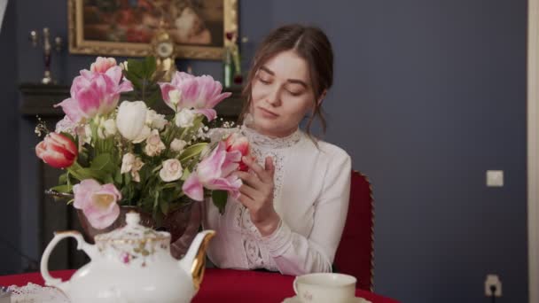 Hermosa chica sentada en una habitación con un interior vintage y disfruta del aroma de los tulipanes fragantes — Vídeo de stock