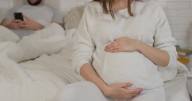 Kocasının arka planında yumuşak pijamalı hamile bir kızın yakın plan fotoğrafı.