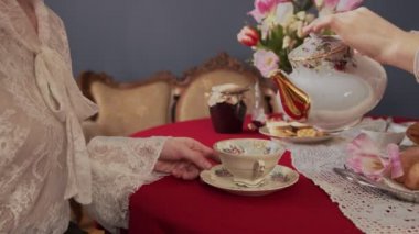 Kırmızı bir masa örtüsü üzerindeki eski bir bardağın çerçevesini yavaşça çay ile doldurun.