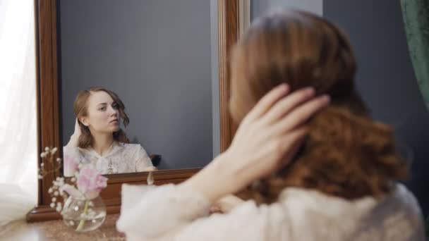 Chica suavemente trenzas su cabello mirando en un espejo vintage — Vídeos de Stock