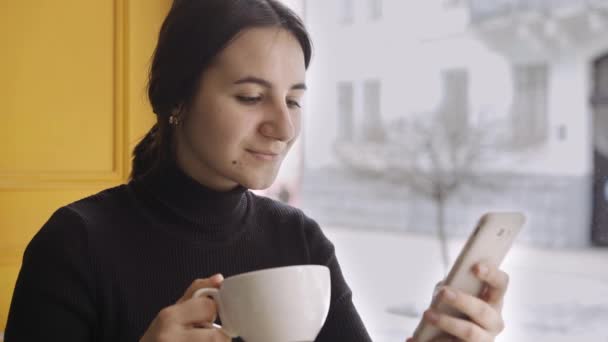 Девушка сидит за столом в кафе и пьет ароматный кофе — стоковое видео