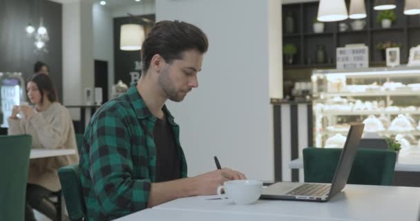 Joven chica bonita notó a un chico joven trabajando en su computadora portátil en un café — Vídeos de Stock