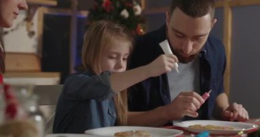 Küçük kız, babasına zencefilli çörek süslemesinde yardım etmek için ayarlamalar yapıyor.