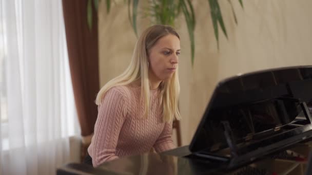 Jeune fille attrayante avec de longs cheveux blonds et beaux yeux bleus aime jouer du piano — Video