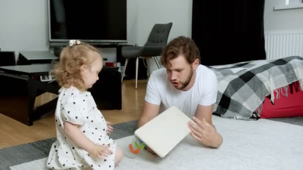Ein junger Vater erklärt seiner zweijährigen Tochter, wie man mit einem Spielzeug spielt — Stockvideo