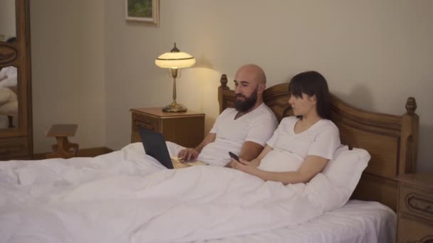 Młodzi ludzie leżą w łóżku i wybrać przytulne miejsce na relaks — Wideo stockowe
