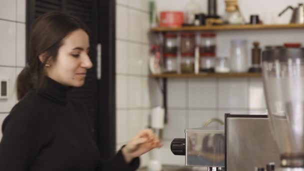 Девушка включает кофеварку и робко смотрит в камеру — стоковое видео