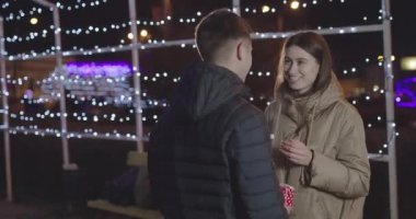 Genç çift, şehir merkezinde mavi ışıkların altında Sevgililer Günü için hediyelerini değiş tokuş ediyor.