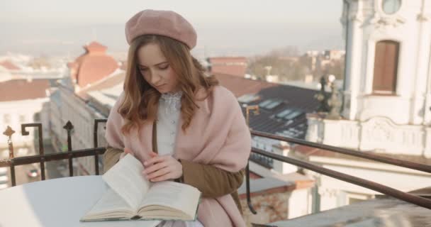Портрет молодої тендітної дівчини, яка насолоджується часом, проведеним на самоті, читаючи книгу і захоплюючись пейзажами — стокове відео