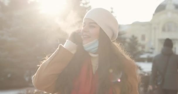 Крупным планом красивая симпатичная девушка прогуливается по зимнему городу в карантине и разговаривает по телефону — стоковое видео