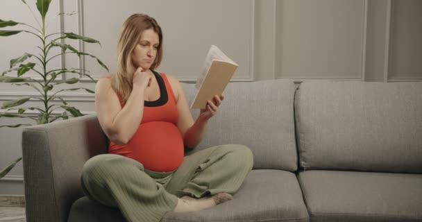 Uma mulher grávida está lendo um livro sobre como ser uma boa mãe. — Vídeo de Stock