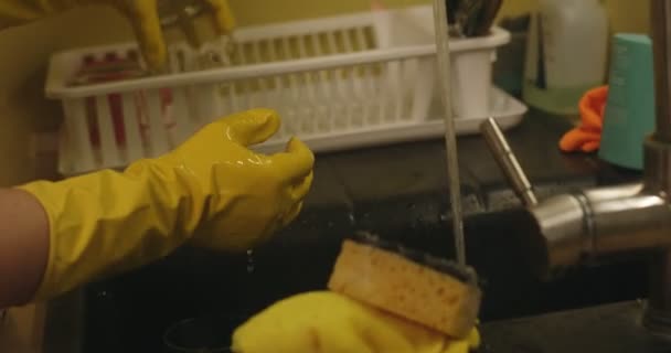 Женские руки моют посуду. Руки в жёлтых резиновых перчатках, мытье чашки с мочалкой в раковине. — стоковое видео