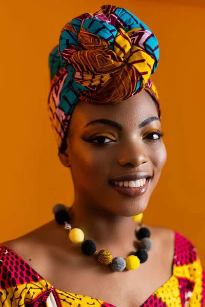 Vertical photo of a black woman in a bright turban and with a necklace around her neck.