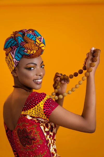 Femme africaine en vêtements nationaux et avec un foulard. Elle tient des bijoux dans ses mains. — Photo