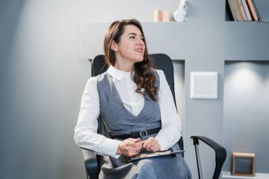 Kız iş kıyafetleri giyiyor. İş kadını ofiste bir sandalyede oturuyor..