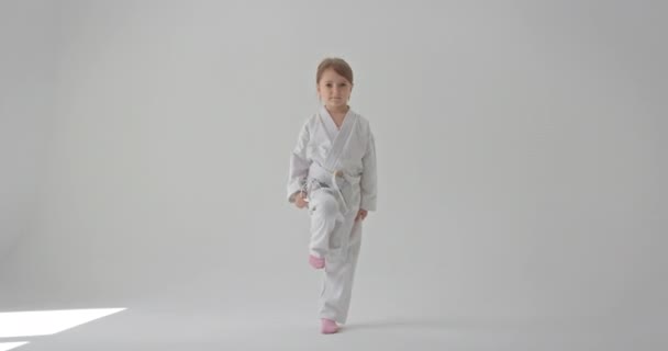 Ein kleines Mädchen im Kimono tritt und blickt in die Kamera. Tritt mit einem Fuß. — Stockvideo