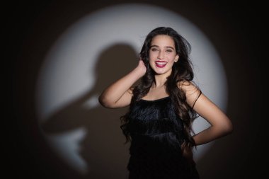 Hollywood gülüşlü bir kız kameraya gülümsüyor. Sahne ışığı. El kafaya bastırılır..