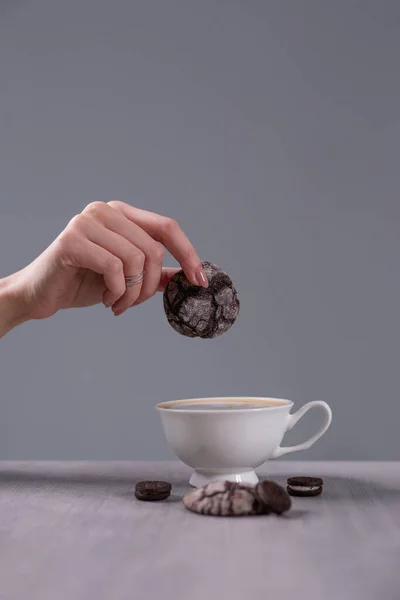 Cup of cappuccino on the table. The girl holds a cookie over a cup. Coffee with pastries is tastier. — Stock Photo, Image