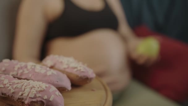 La mujer embarazada abandona sus pasteles favoritos y elige una manzana. Es más útil para el niño.. — Vídeo de stock