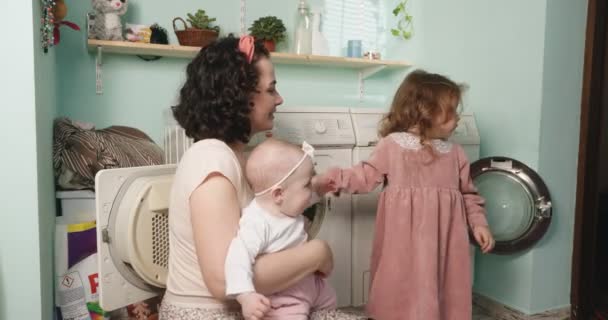Домашние обязанности многодетной матери. Мама и дочери положили грязную одежду для стирки. — стоковое видео