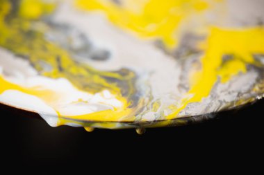 Siyah arka planda yuvarlak bir plakadan damlayan boya. Karışık gri-sarı boya aşağı akıyor..