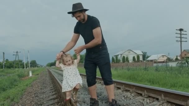 Pappa och dotter går på järnvägen. En promenad genom byn under karantänen. — Stockvideo