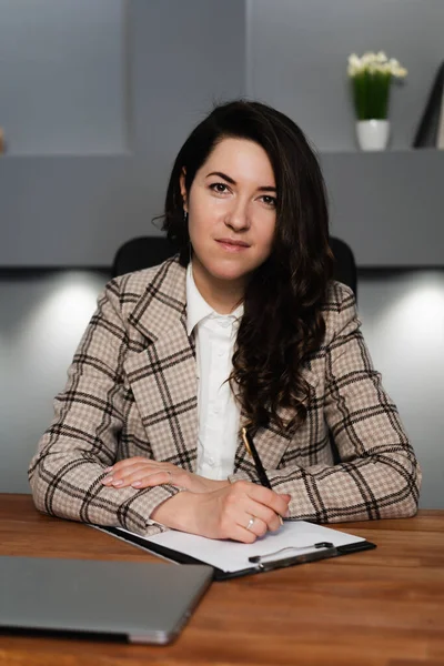 İş kadını masada oturuyor. Masanın üzerinde notlar için kağıda yazılmış bir defter var. Kız ceket giyiyor..