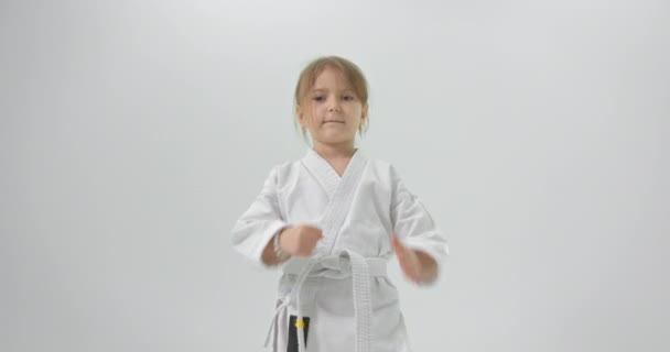 L'enfant est accueilli au karaté. La fille dans un kimono et sur un fond blanc regarde la caméra et est accueillie. — Video