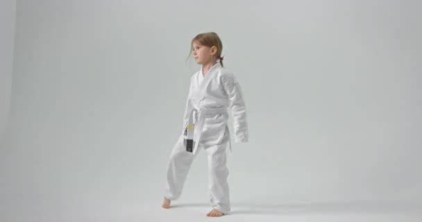 The child puts his hands on his belt and raises his leg high in the air. A girl who practices karate. — Stok video