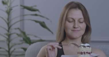 A woman appetizingly eats a piece of cake with a fork and holds it in her hands.