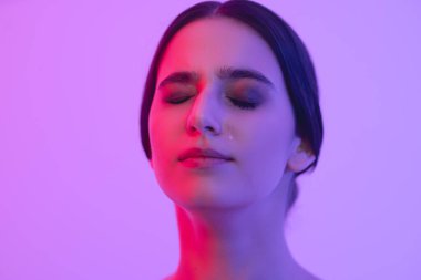 Girls face with a tear on her cheek in pink light. Face close up.