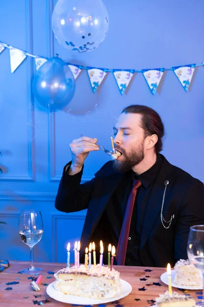 A man eats a cake with his eyes closed at the table. Celebration alone.
