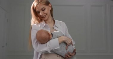 Bebek annesinin kollarında uyuyakaldı. Annem bebeği kucağında tutuyor ve gülümsüyor..