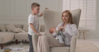 Büyük oğul vitamin alırken küçük kardeş uyuyor ve annesinin kollarında. Aile evde vakit geçirir..