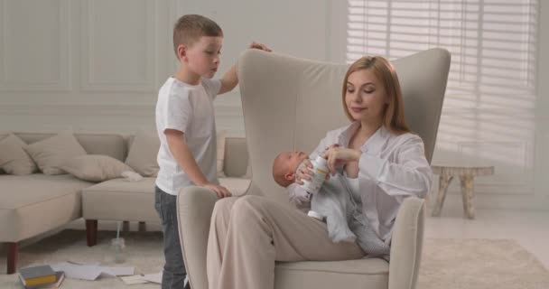 De oudere zoon neemt vitaminen terwijl de jongere broer slaapt en is in de moeders armen. Het gezin brengt tijd thuis door. — Stockvideo