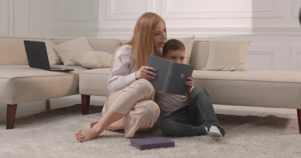 Mãe e filho lêem livros em casa. Mãe abraça seu filho e lê-lhe um conto de fadas. — Vídeo de Stock