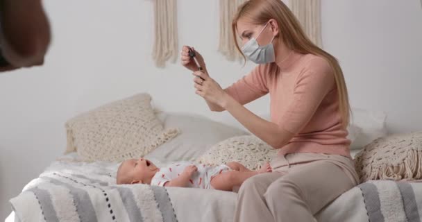 La mère donne des vitamines à l'enfant à travers une pipette. La mère dans le masque prend soin de la santé des enfants. — Video