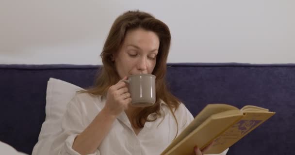 커피 한 잔 과 손에 책을 들고 혼자 서 긴장을 푸는 여성 — 비디오