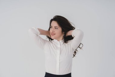 Beyaz gömlekli kız elleri başının arkasında. Beyaz arka planda genç bir kızın fotoğrafı..