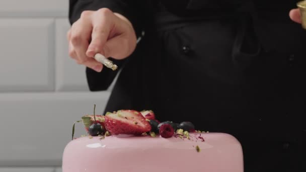 El confitero decora un pastel de mousse rosa con pistachos y fruta fresca. — Vídeo de stock