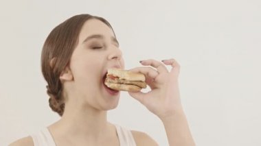 Kız bir burger tutuyor ve yiyor. Hızlı abur cubur alımı.