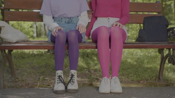 Яркие колготки на ногах девочек-подростков, сидящих на скамейке в парке. Детали в стиле одежды. — стоковое видео