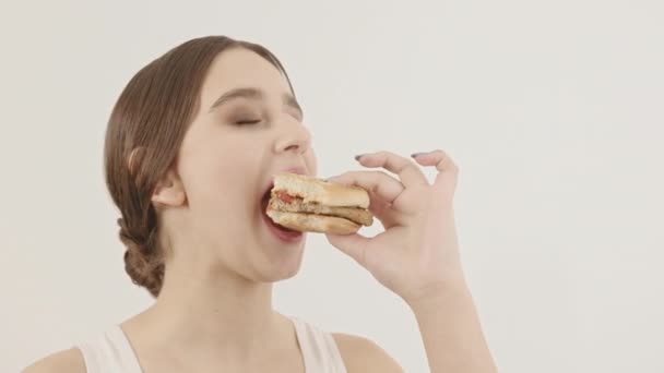 La chica sostiene una hamburguesa y se la come. Consumo rápido de comida chatarra. — Vídeos de Stock
