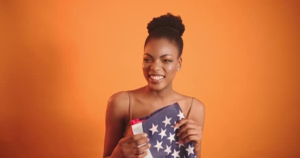 Ένα μαύρο κορίτσι κρατά μια σημαία στα χέρια της και χαμογελά στο πλάι. Χαμογελαστό μαύρο κορίτσι με σημαία της Αμερικής. — Αρχείο Βίντεο