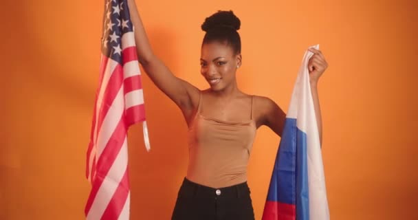 Ένα μαύρο κορίτσι κρατάει δύο σημαίες, μια Ρωσίδα και μια Αμερικανίδα, και διαλέγει έναν Αμερικάνο. Επιλογή χώρας από ένα μαύρο κορίτσι. — Αρχείο Βίντεο