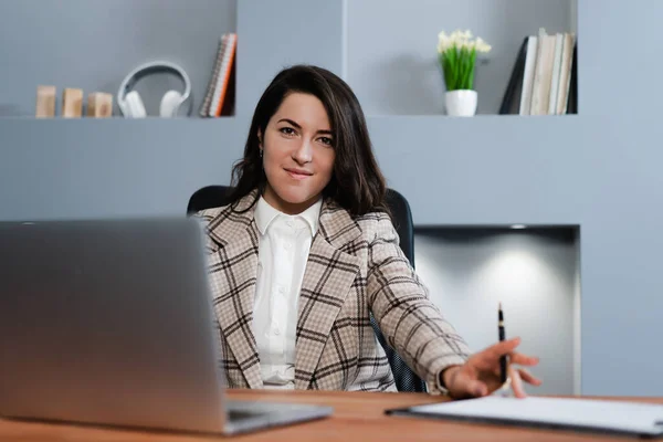 Bizneswoman za laptopem, trzymając długopis i patrząc surowo w kamerę. — Zdjęcie stockowe