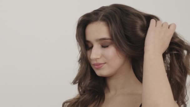 La chica con un hermoso maquillaje endereza el cabello con una mano. — Vídeos de Stock