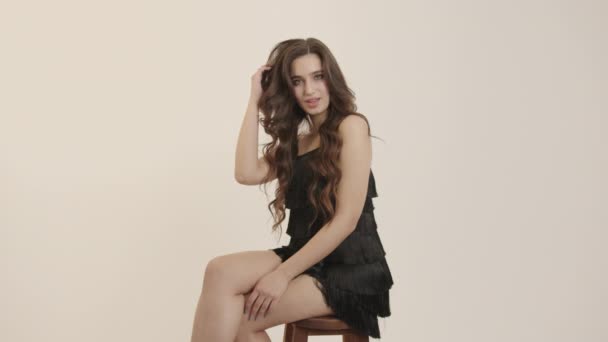 Krásná bruneta sedí na židli a narovnává dlouhé vlnité vlasy. — Stock video
